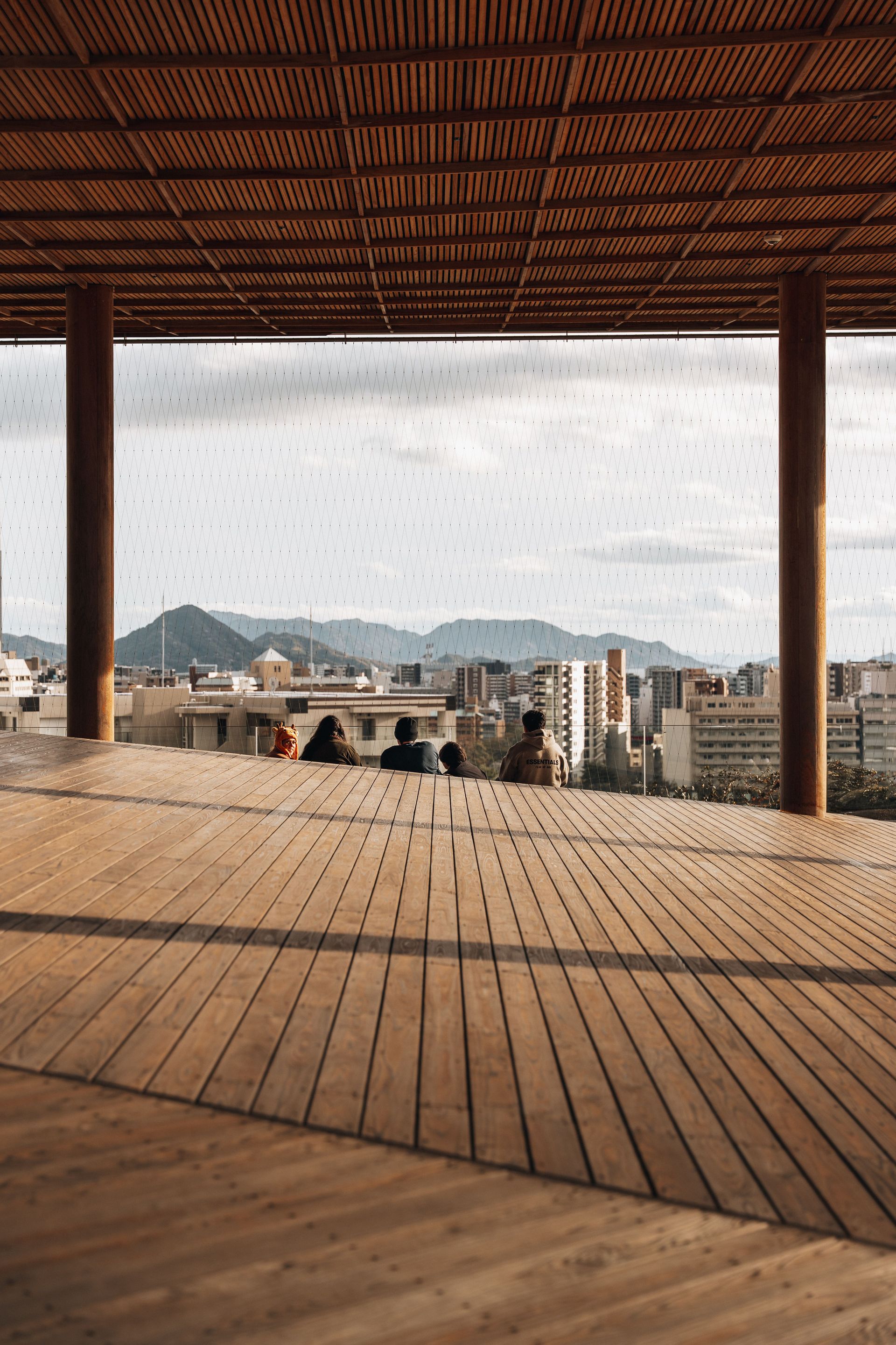 A serene view from a wooden terrace in Hiroshima, showcasing the city skyline and distant mountains.